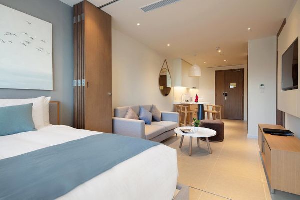 giường màu trắng có khăn xanh, có bộ sofa và bàn gỗ nhỏ