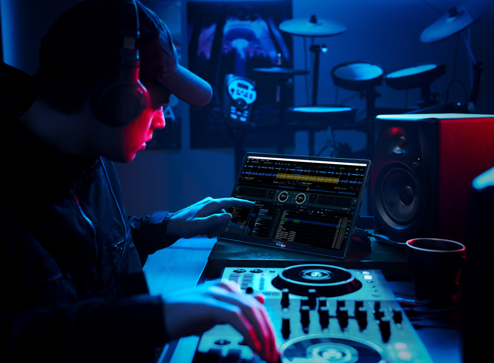 Man using the Flow Z13 touchscreen for music editing, seated at a mixing station, wearing headphones, with a drumset and speakers in the background.